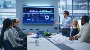 A diverse team of UK business professionals collaborating around a large screen displaying an online learning course dashboard, signifying corporate training.